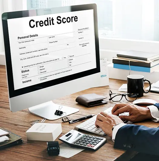 Person reviewing a credit score form on a desktop computer with a calculator and documents on the desk
